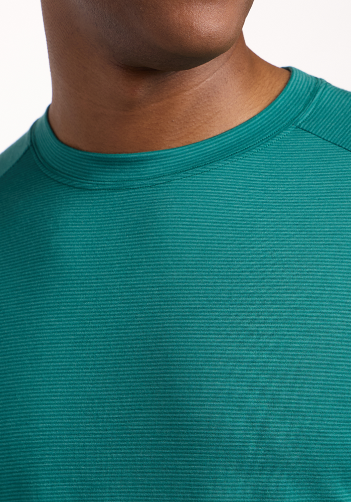 Close-up of a person wearing the Woolx Essential Tee - Woodland Mini Stripe, featuring a teal ribbed crew-neck design. Only the lower half of the face, neck, and upper chest are shown against a plain background.