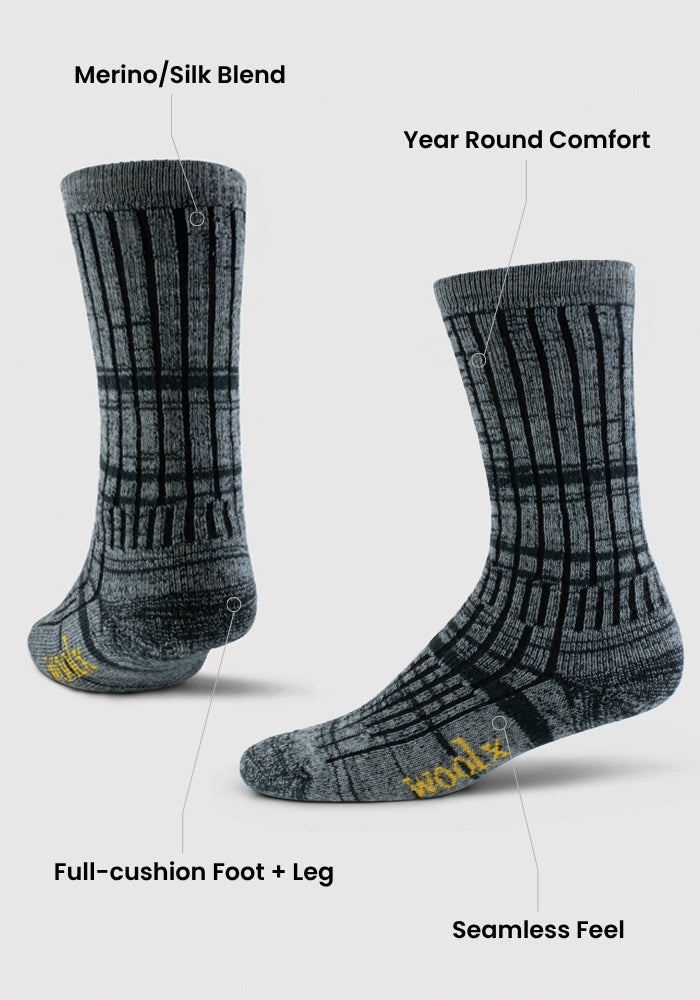 Two warm violet mid-calf Woolx socks are shown with black geometric patterns, featuring moisture-wicking Merino wool/silk blend, year-round comfort, full-cushion foot and leg, seamless feel, and "Woolx" in yellow on the toes.