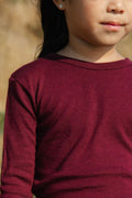 Close-up of a child wearing a maroon long-sleeve shirt with a blurred natural background