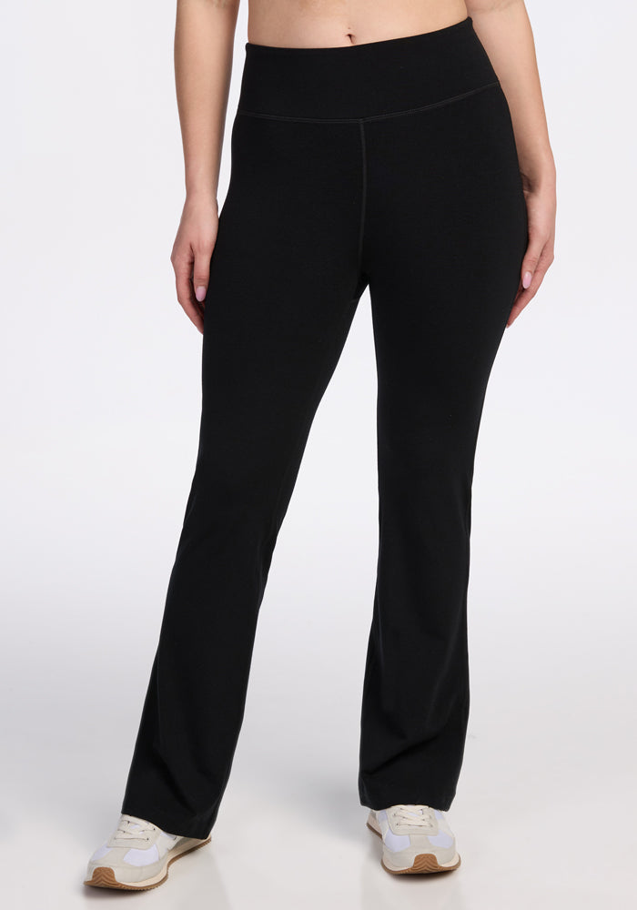 Wearing Woolx’s Morgan Flare Pants in black, a person stands against a plain white background, visible only from midriff to feet, paired with white sneakers. | Ariana is 5'11", wearing a size S