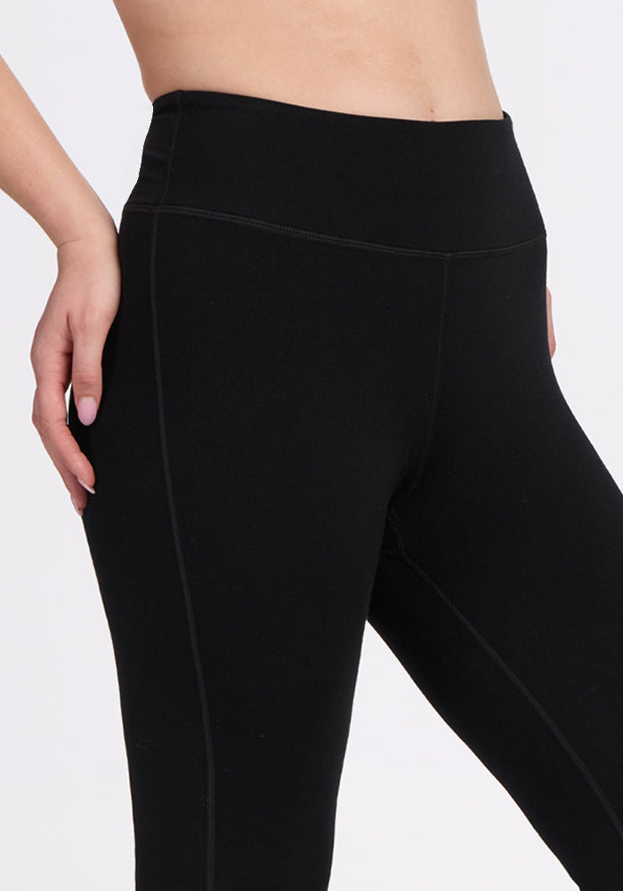 A person wearing Woolx Morgan Flare Pants in black, shown from midriff to upper thighs, with one hand on their hip against a plain white background.